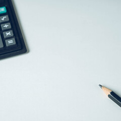 Close-up of black pencil and calculator on empty white paper blank. Top view.