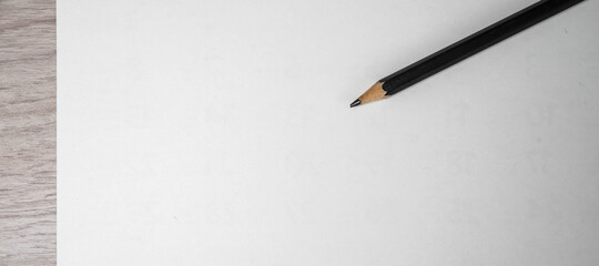 Close-up of pencil on clean white paper blank. Wooden table background. Top view.