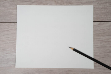 Close-up of pencil on clean white paper blank. Wooden table background. Top view.