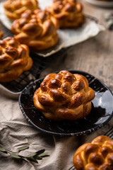 Homemade brioche knot buns on black plate and cooling rack on wooden table. 