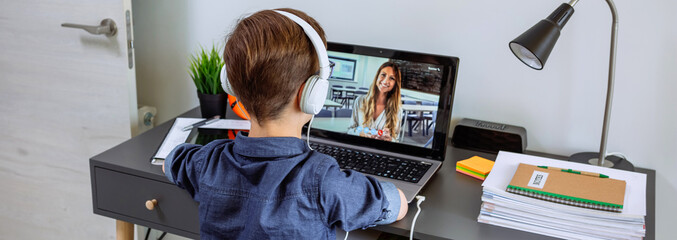 Unrecognizable boy with headphones receiving class at home with laptop from his bedroom. Home schooling concept