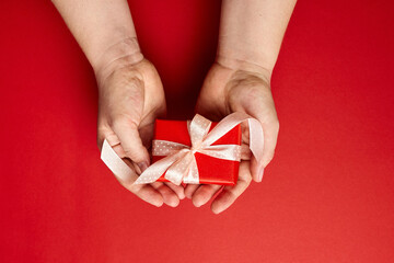 Gift box with ribbon in female hands on red background