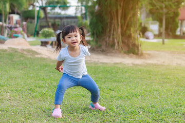 Fototapeta premium Happy Asian baby girl running or jumping and playing at the park or garden field. She smiling and laughing. Child aged 2-3 years old. Relaxation and exercise for health. Development of kid concept.