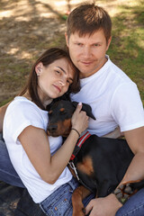 couple in love, man and woman, hugging beloved dog or doberman in summer park