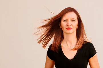 Casual home office profile picture. Portrait photo of pretty middle age business woman in black top standing in front of house, her ginger burgungy red hair flying in the air around her face.