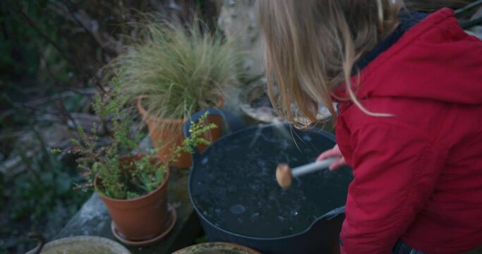 A little preschooler is using a toy hammer to break the ice on some buckets in the garden