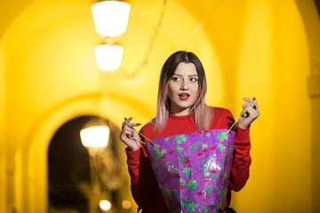 Bella ragazza bionda con maglione rosso guarda con stupore cosa c'è dentro una busta da shopping,...