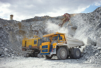 Heavy mining dump truck at the time of loading the large stone fragments in a limestone quarry, close-up.