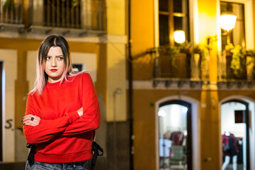 Bella ragazza bionda con maglione rosso incrocia le braccia con aria severa, in contesto urbano