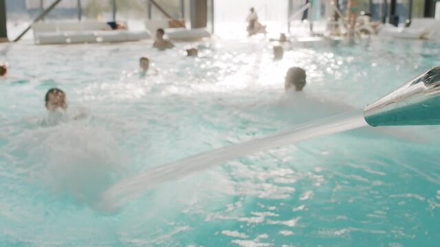 Slow-motion footage of people having good time in thermal pool with hydromassage splashing water everywhere