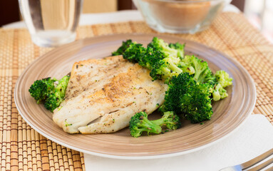 fried fillet of sea bass with garnish of broccoli on black warm stone plate
