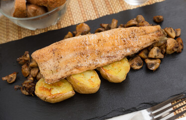 fried trout fillet on pillow of fried champignon mushrooms on dark warm stone plate