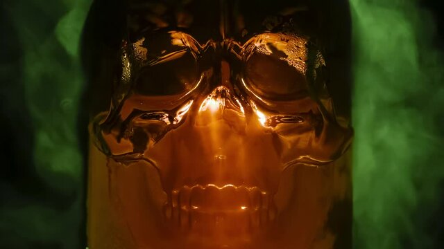 Glass Skull in Poisonous Fumes. Ice skull glowing with golden brown light in the poisonous vapors of evaporating green gas. Slow Motion 240 fps