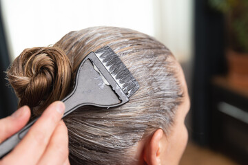 Hairdresser applying bleach or hair color for hair dye with a black brush at home or salon.