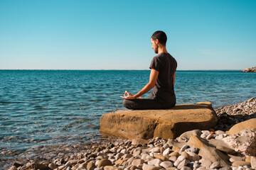Attractive young man practicing yoga meditation and breathwork outdoors by the sea