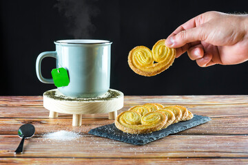Hand of a person holding a cookie ready to eat with a cup of hot tea. Sugar sprinkled on the table