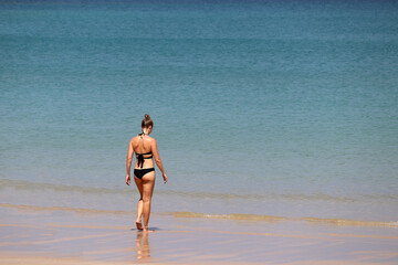 Fototapeta na wymiar Vacation on the beach, slim woman in bikini go swimming to the azure sea