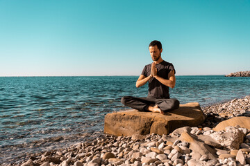 Attractive young man practicing yoga meditation and breathwork outdoors by the sea
