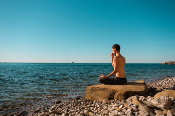 Attractive young man practicing yoga meditation and breathwork outdoors by the sea