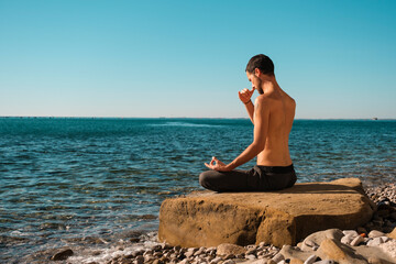 Attractive young man practicing yoga meditation and breathwork outdoors by the sea