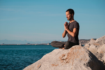 Attractive young man practicing yoga meditation and breathwork outdoors by the sea