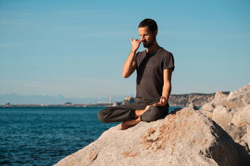 Attractive young man practicing yoga meditation and breathwork outdoors by the sea