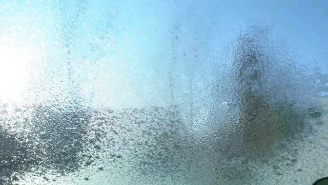 Closeup view 4k video of texture of frost on glass of window of automobile. Driver uses special defroster spray liquid to easy remove frost from windshield