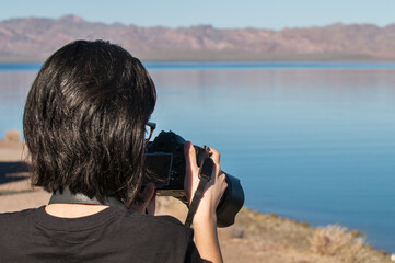 Teenager holding a digital camera in front of the sea of Cortes taking a landscape photography