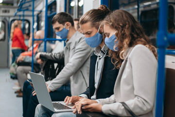 subway passengers wearing protective masks using their laptops.