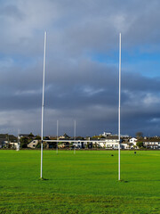 Tall goal post for Irish National sport rugby, hurling, gaelic football and camogie on a green training pitch, blue cloudy sky. Galway city in the background.