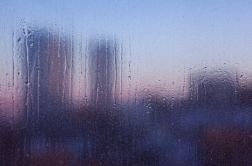 View of the city through icy glass. Winter pink sunset. Icy window at sunset as abstract background
