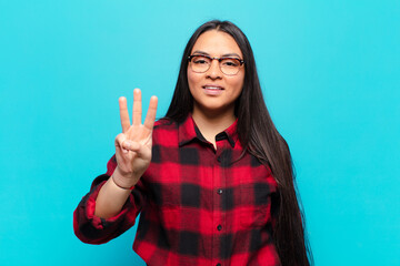 latin woman smiling and looking friendly, showing number three or third with hand forward, counting...