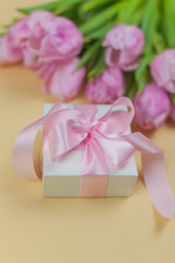 Gift box with ribbon, bouquet of pink tulips on a beige background. Mothers Day. International Women's Day. Holidays.
