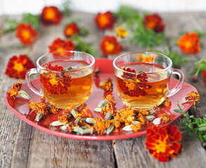 Alternative medicine. Tea cups with herbal tea with calendula flowers or Chernobrivtsi or Mary's Gold on a red plate on a vintage wooden background with dried flowers. Herbal tea benefits your health.