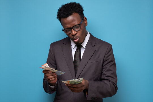 African man in suit holding and counting money. Studio shot on blue wall.