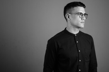 Young handsome businessman wearing eyeglasses against gray background