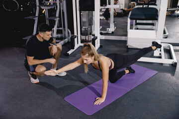 The coach checks the correctness of the exercise on the feet in the gym. Training in the gym is a small group. A man and a girl train together.