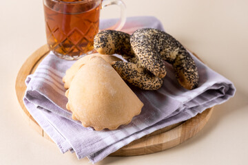 Variety of Tasty Homemade Buns on Pink Napkin Cup of Tea Wooden Tray Light Yellow Background Horizontal