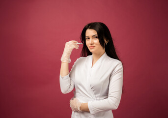 a beautician in a white suit and transparent gloves holds a botox syringe on a burgundy background with space for text