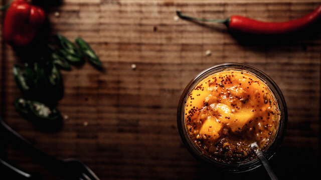 Mango Chutney in einem Glas und L&ouml;ffel auf einem Holzbrett stehend, im Hintergrund frischer Chili.