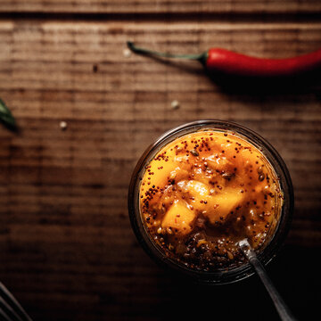 Mango Chutney in einem Glas und L&ouml;ffel auf einem Holzbrett stehend, im Hintergrund frischer Chili.