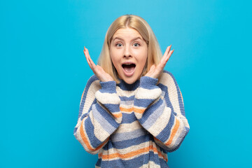 blonde woman feeling shocked and excited, laughing, amazed and happy because of an unexpected...