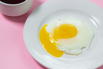 Scrambled eggs on a pink background. Fried eggs on a white plate. Delicious breakfast with a cup of coffee.