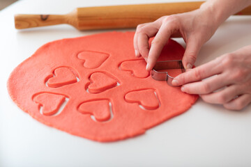 A woman makes homemade Valentine's Day cookies from shortcrust pastry in the form of red hearts.