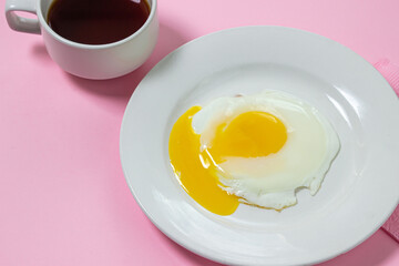 Scrambled eggs on a pink background. Fried eggs on a white plate. Delicious breakfast with a cup of coffee.