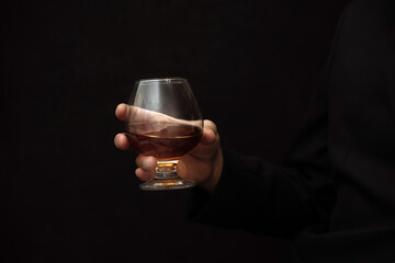 glass of alcoholic drink, hold cognac in hands on a dark background