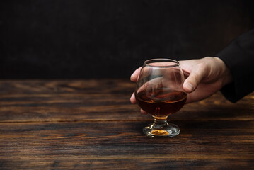 glass of alcoholic drink, hold cognac in hands on a dark background