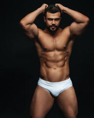 Latin hunk in white swimwear at black background