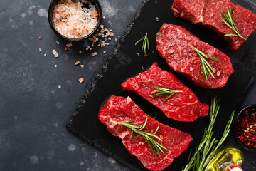 Beef meat. Four fresh raw beef steak with spices, onions and rosemary on dark slate or concrete background. Top view.