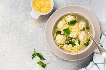 Bowl of traditional Italian soup with chicken meatballs and egg paste, Parmesan cheese, parsley on gray table background. Traditional Italian kitchen. Top view.